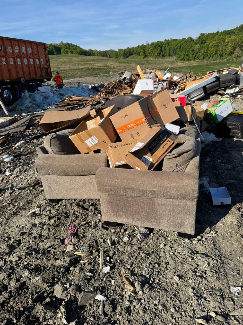 Abandoned couch surrounded by cardboard boxes at a waste disposal site.