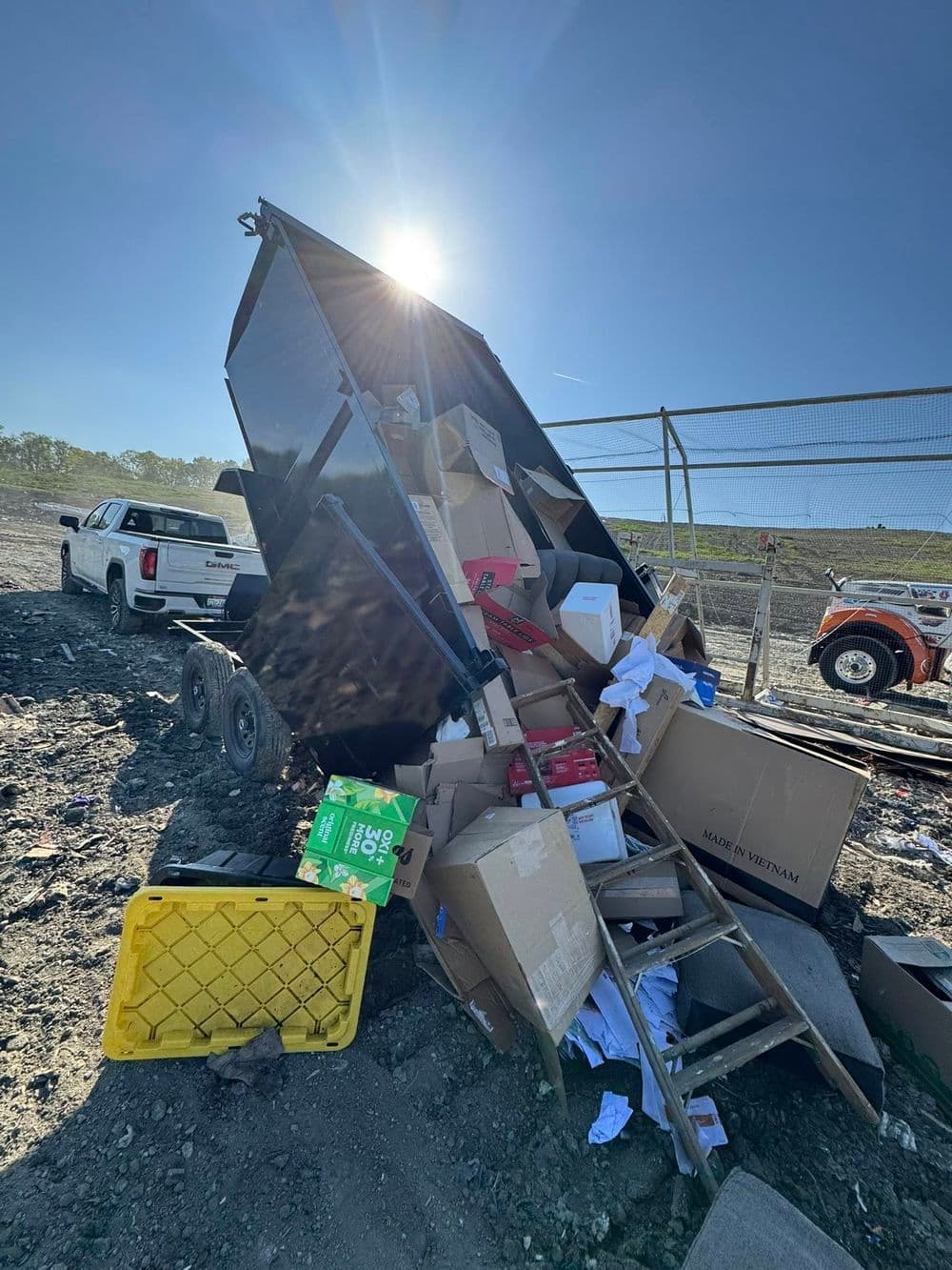 Overflowing dumpster with cardboard boxes and construction debris under sunlight.