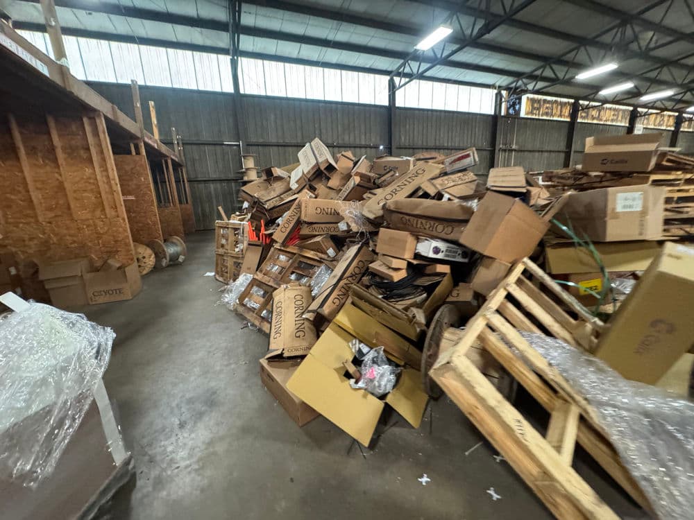 Large pile of cardboard boxes and pallets in a warehouse setting. Cluttered industrial space.