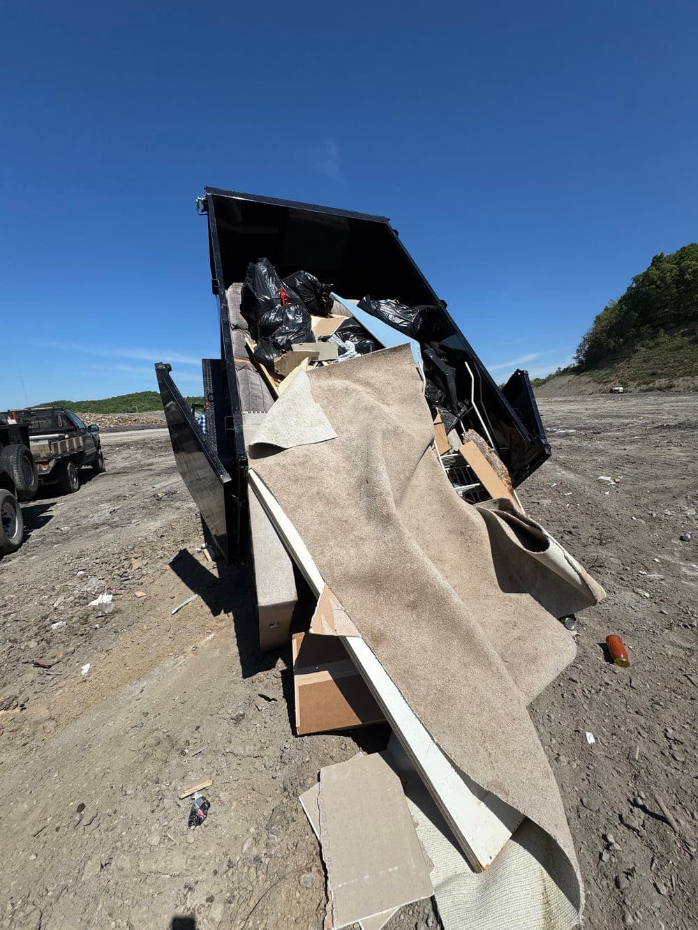 Dump truck filled with assorted debris, including carpet and cardboard, at a waste disposal site.