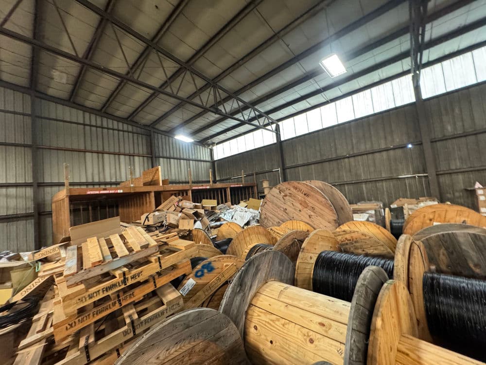 Wooden spools and pallets stacked in a large industrial warehouse interior.