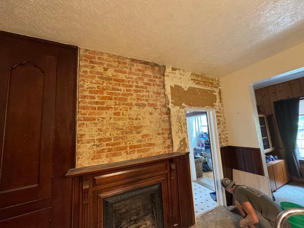 Renovation process showing exposed brick wall and a worker removing old wallpaper.