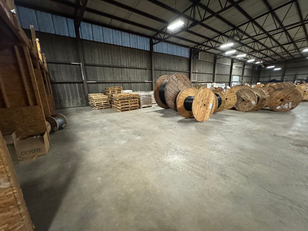 Warehouse interior with wooden reels and pallets stacked on the floor, showcasing industrial storage.