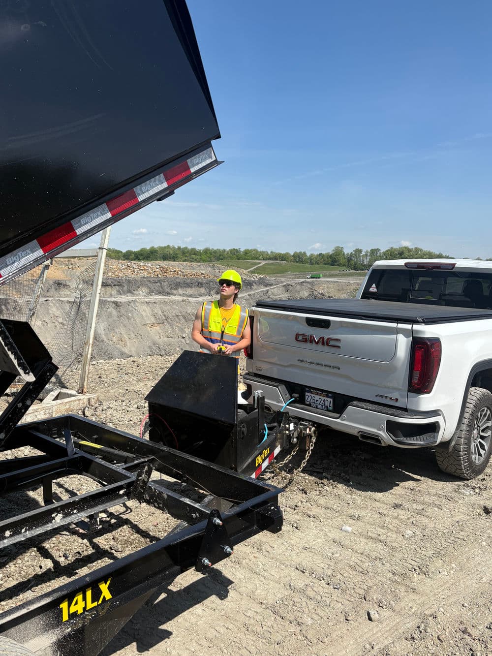 Construction worker in safety gear operating a dump trailer attached to a GMC truck.