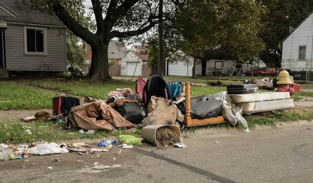 Debris and discarded furniture clutter a residential street in a neglected neighborhood.